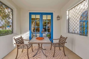 Un balcón con mesa y sillas, una puerta azul y barandillas decorativas de hierro.