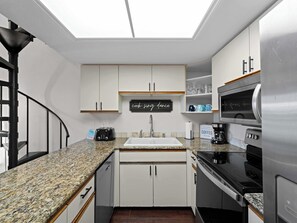 A compact kitchen with white cabinets, a granite countertop, a built-in oven, and a stainless steel refrigerator.