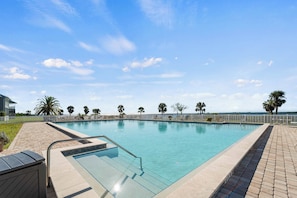 A rectangular swimming pool with a glass edge, surrounded by a brick deck and a white fence.