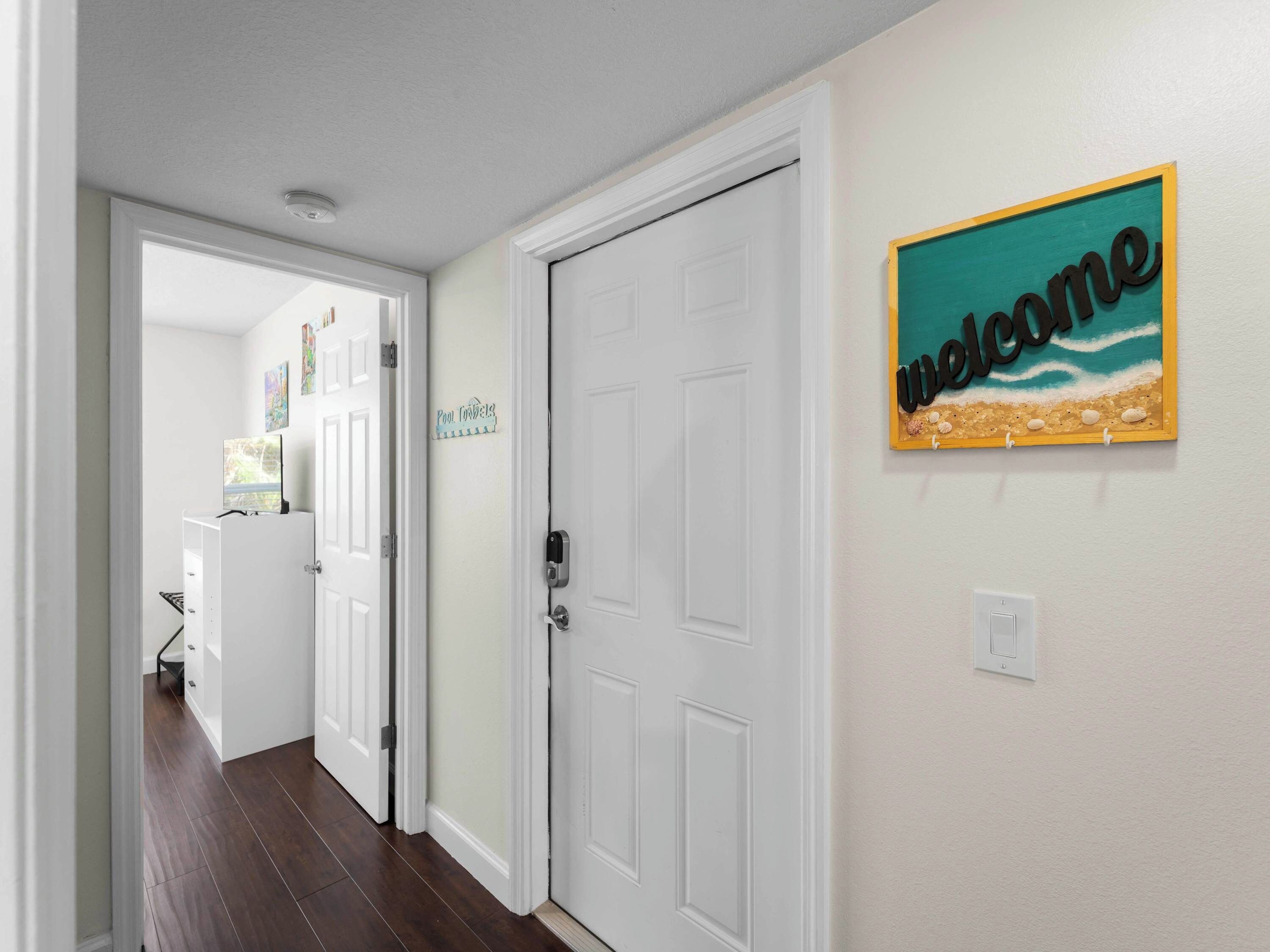 A hallway with a white door, a welcome sign, and a sign indicating a pool.