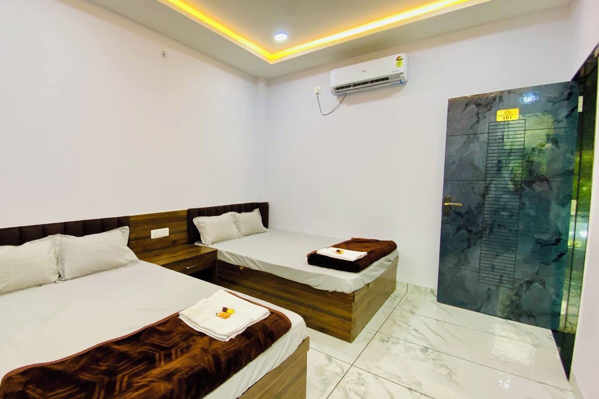 A hotel room with two beds, a bathroom with a glass shower, and an air conditioning unit on the wall.