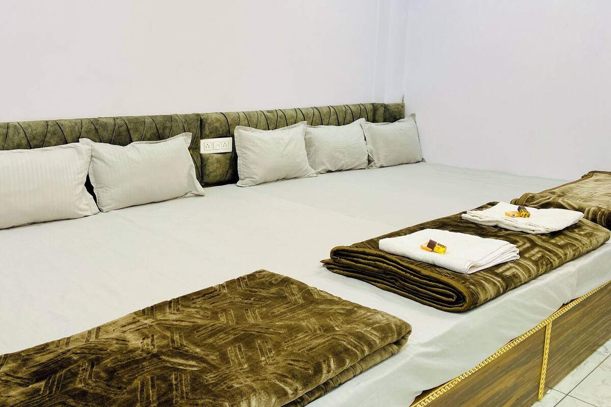 A neatly made bed with white bedding and brown decorative pillows, a bedside table with a power outlet, and a folded towel with a toothbrush on it.