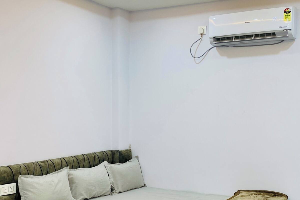 A bedroom with a bed, pillows, a blanket, an air conditioner, and a ceiling fan.