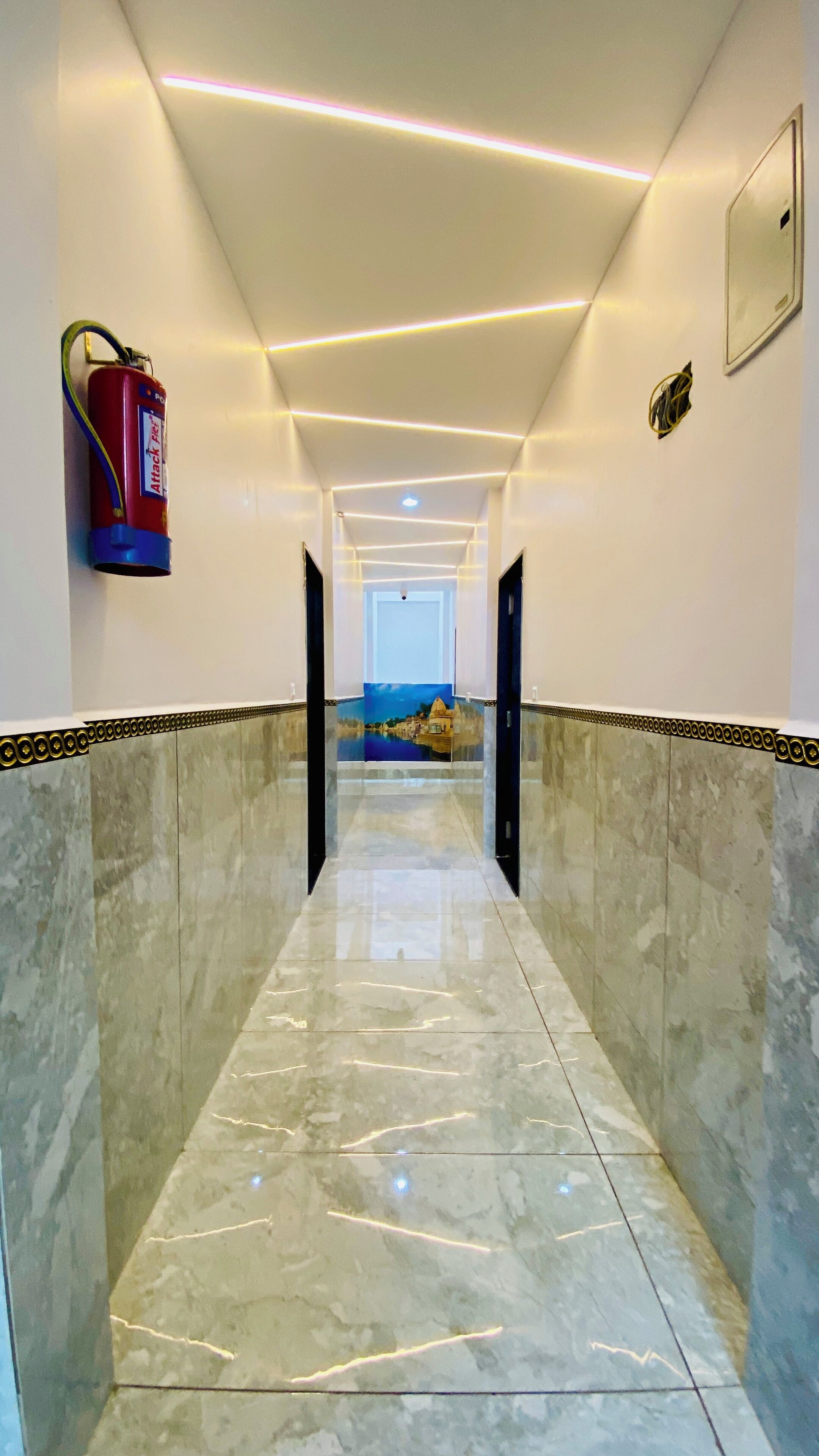 A hallway with a fire extinguisher mounted on the wall, a door at the end, and a view of a landscape through the glass wall.