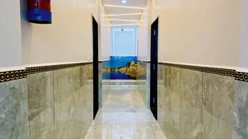 A hallway with a fire extinguisher mounted on the wall, a door at the end, and a view of a landscape through the glass wall.