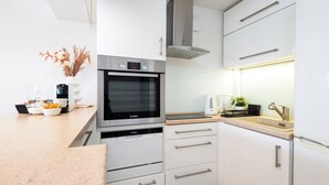 Une cuisine moderne avec des meubles blancs, des appareils en acier inoxydable et un plan de travail sur lequel se trouvent une machine à café et des bols.