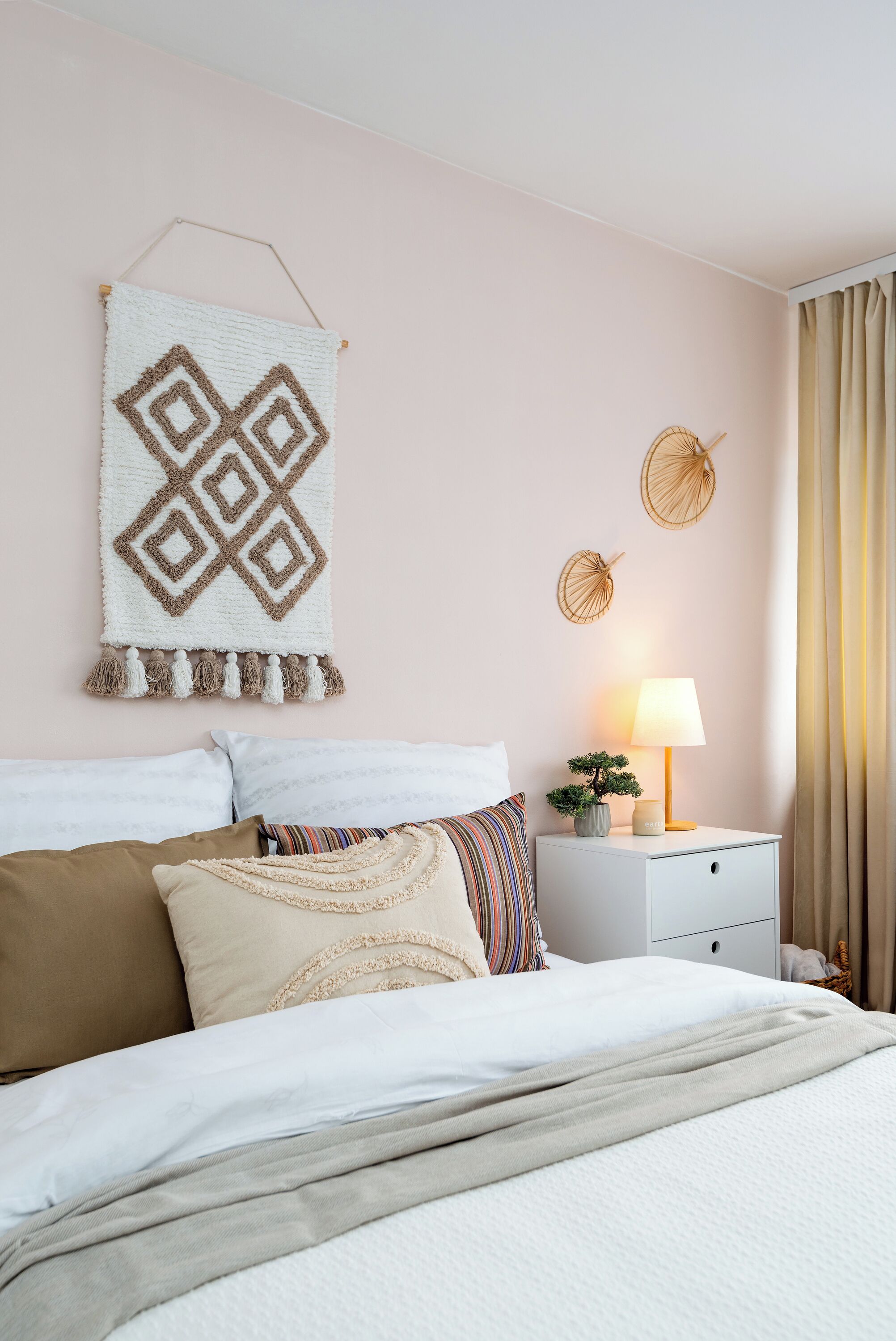 A neatly made bed with a white and beige blanket, a bedside lamp, and a wall hanging.