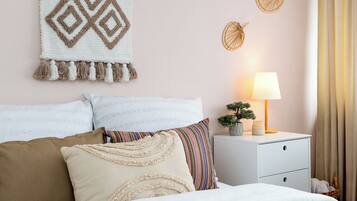 A neatly made bed with a white and beige blanket, a bedside lamp, and a wall hanging.