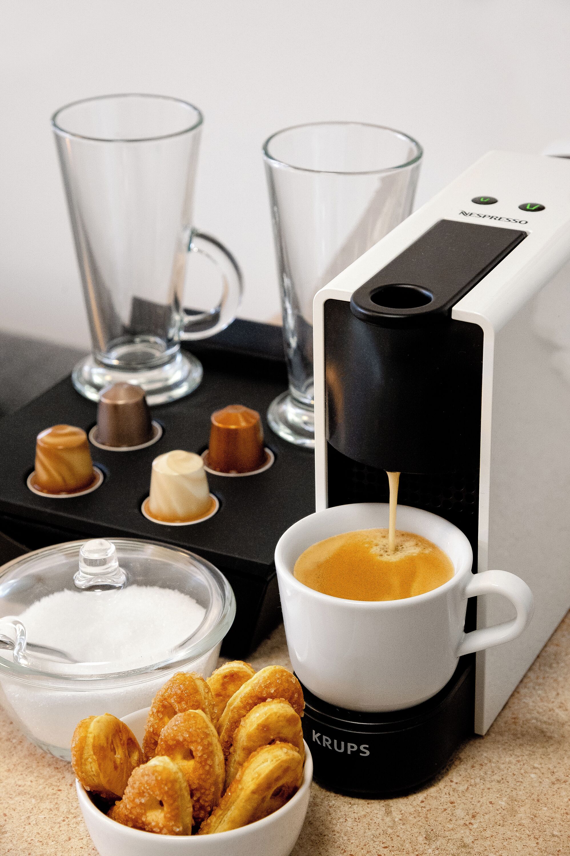 Une machine à café qui verse du café dans une tasse, un bol rempli de viennoiseries et un verre d’eau, le tout posé sur un comptoir.