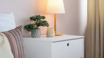 Una camera da letto ordinata con un comodino bianco, una lampada da comodino, un piccolo vaso con una pianta e due ventole decorative a parete.