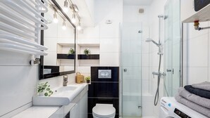 Une salle de bain moderne avec un lavabo blanc, des toilettes, une douche en verre et un lave-linge.
