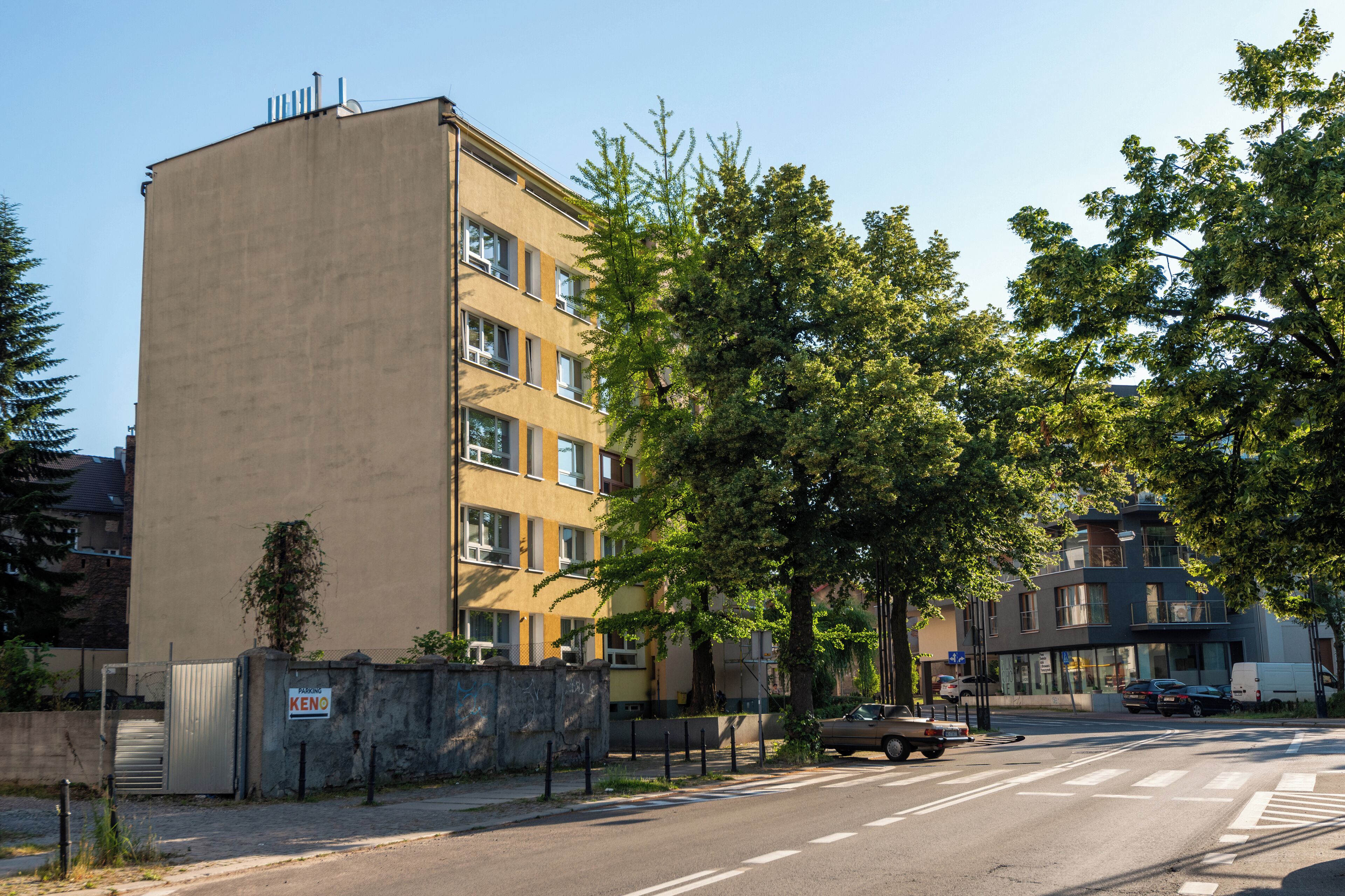Un edificio de varios pisos con fachada plana, entrada protegida por una reja y una calle delante.