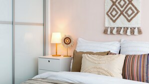 Un lit bien fait, avec une couette blanche et des oreillers, une lampe de chevet et une décoration murale à motifs géométriques.