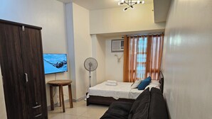 A bedroom with a bed, a TV, a fan, and a wardrobe. - Cozy studio condo with WiFi, AC in beautiful Makati (Makati)