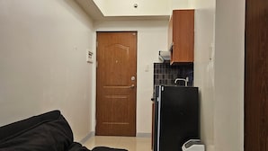 A compact living space with a kitchenette, a wooden door, and a black sofa. - Cozy studio condo with WiFi, AC in beautiful Makati (Makati)