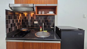A compact kitchen with a stove, sink, and black refrigerator. - Cozy studio condo with WiFi, AC in beautiful Makati (Makati)