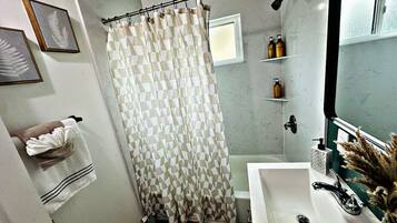 A bathroom with a shower curtain, a sink, a mirror, and a towel rack.