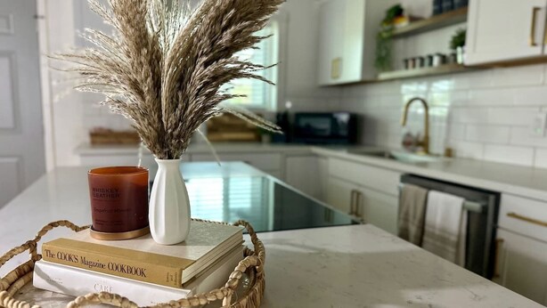 A kitchen counter with a woven tray holding a book, a candle, and dried plants.