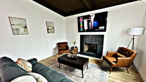 A living room with a sofa, coffee table, armchair, fireplace, and artwork on the walls.
