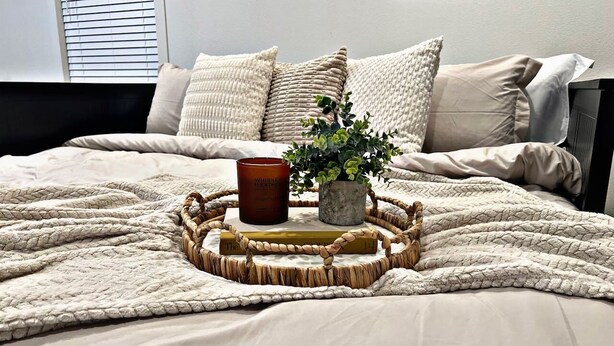 A neatly made bed with a woven tray, a potted plant, and a whiskey bottle. - Sleek+Serene ADU | Modern Kitchen • Outdoor Vibes (Carmichael)