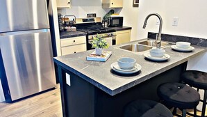 A modern kitchen with a stainless steel refrigerator, a built-in oven, a microwave, and a sink with stools. - Sleek+Serene ADU | Modern Kitchen • Outdoor Vibes (Carmichael)