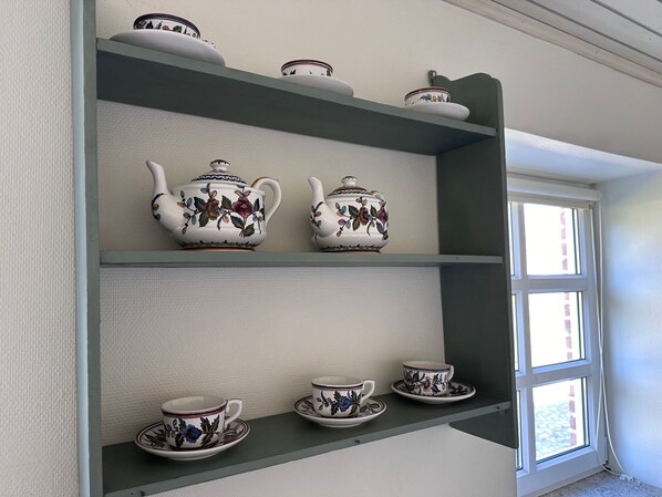 Una estantería con teteras, tazas y platillos de porcelana con motivos florales blancos y azules.