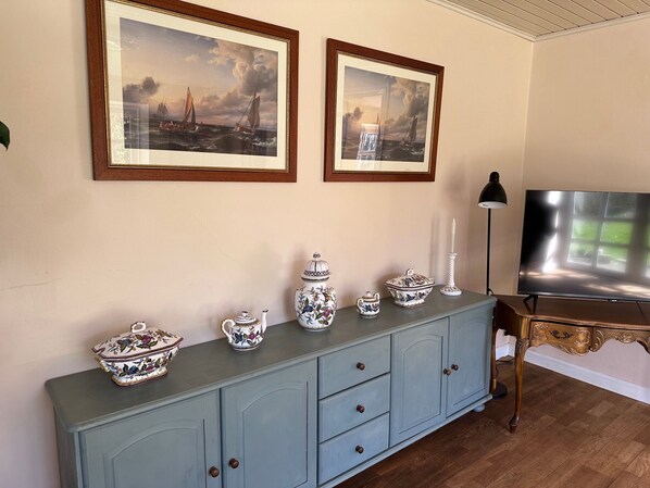 A room with a light blue cabinet, a television, and two framed paintings on the wall. - Æblehuset (Hadsund)