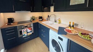 A modern kitchen with dark cabinets, a stainless steel stove, a washing machine, and a countertop with a plate of grapes and crackers.