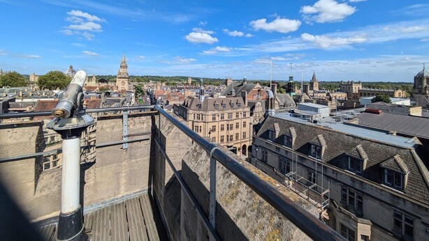 A panoramic view of a historic cityscape with prominent architecture, including a tower and a dome, viewed from a high vantage point.