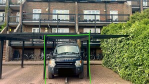 A black Land Rover parked in a covered parking area with a brick building in the background.