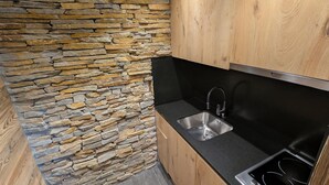 Een keuken met een stenen muur, houten kastjes, een zwart aanrecht en een roestvrijstalen spoelbak.