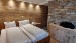 Een slaapkamer met twee bedden, houten paneelwanden, een stenen muur en een houten kast met een zwart jack en een flesje bovenop.