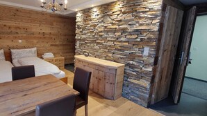 Een kamer met een houten wand, een stenen wand, een bed met witte lakens, een houten tafel en een bank.