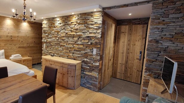 Een slaapkamer met een houten hoofdeinde, een bed met witte lakens, een houten bureau en een stenen muur.