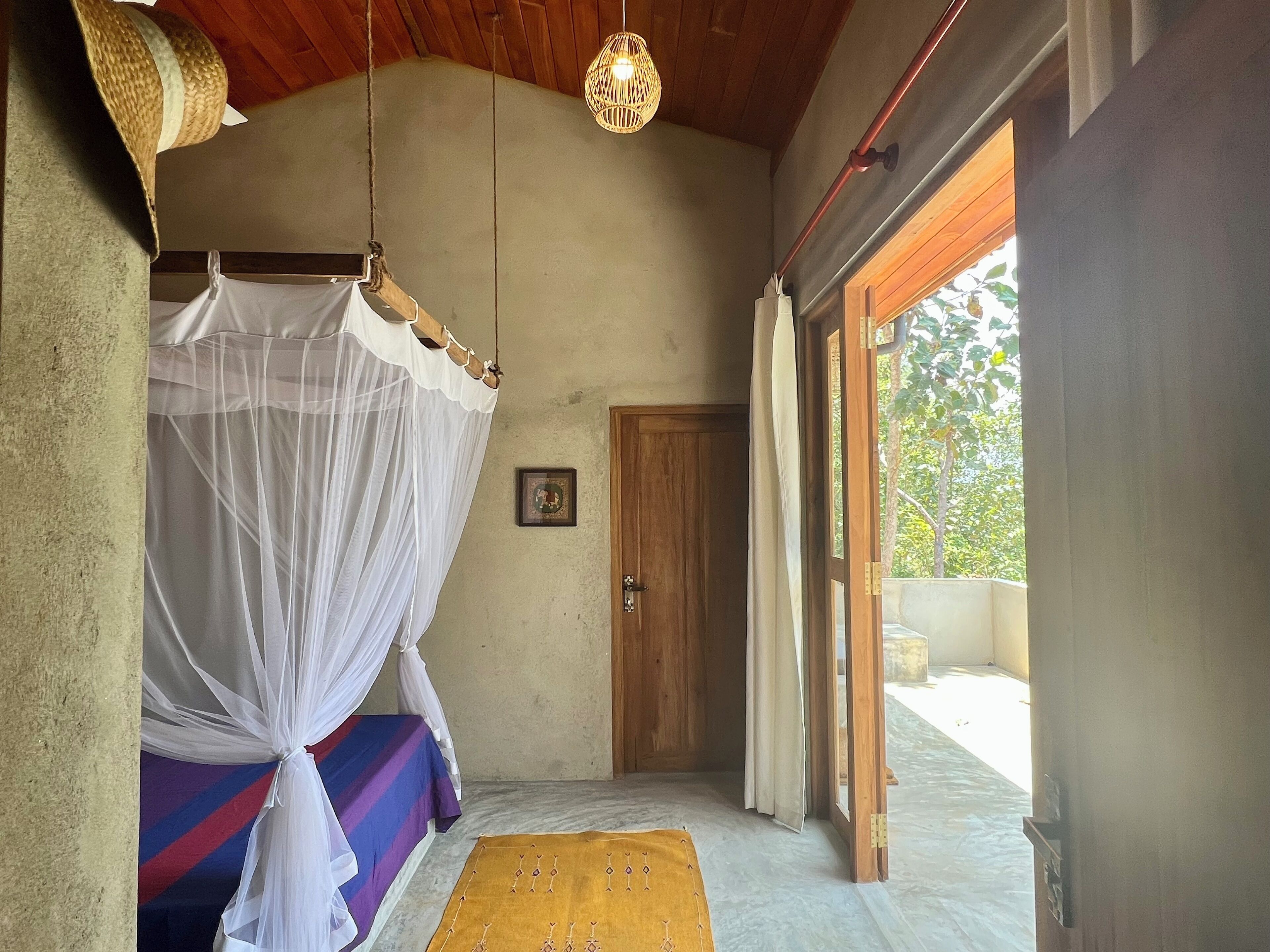 Une chambre à coucher avec un lit, une moustiquaire, une porte en bois et une vue sur l’extérieur.
