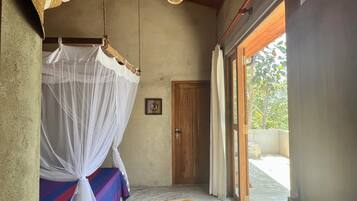 Une chambre à coucher avec un lit, une moustiquaire, une porte en bois et une vue sur l’extérieur.