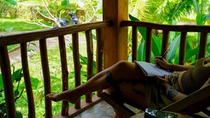 A person sitting on a wooden deck with a view of lush greenery. - Into The Blue Sri Lanka (Tangalle)
