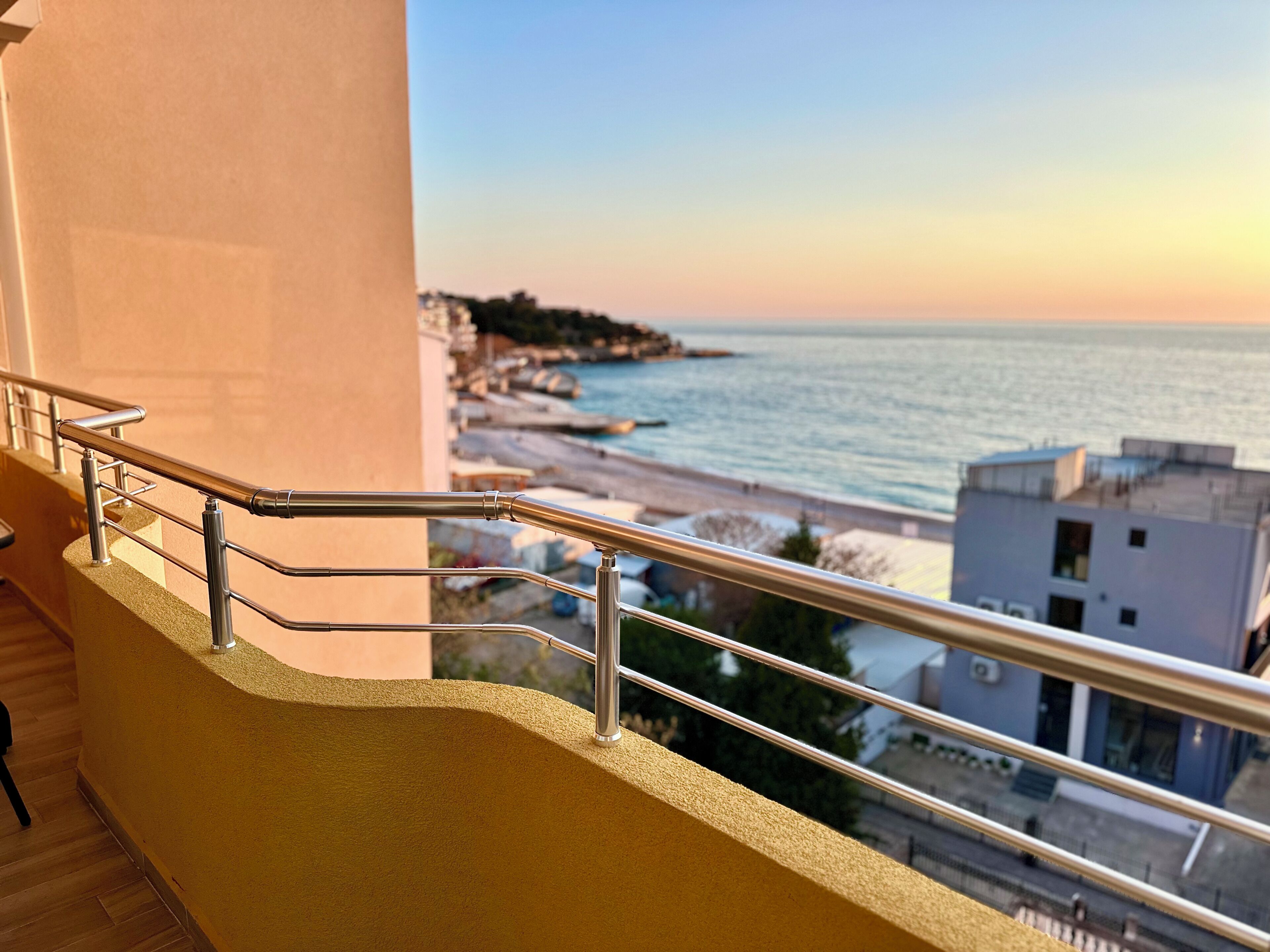 Een balkon met een metalen hekwerk dat uitkijkt op een strand en de oceaan.