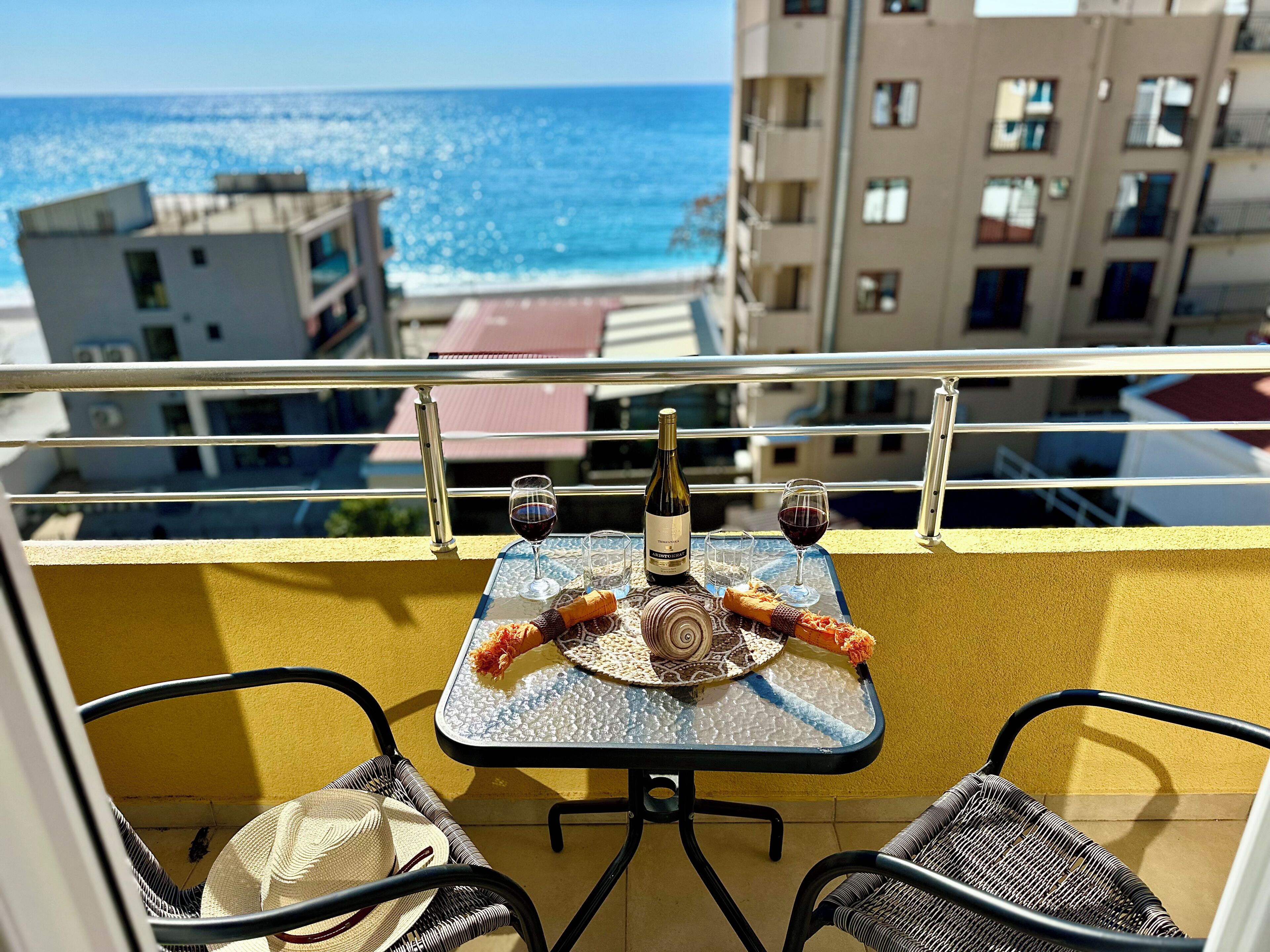 A balcony with a table set for two, a bottle of wine, and a glass of red wine.