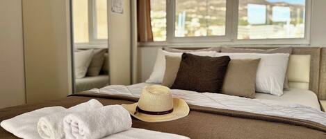 Habitación de hotel con cama, ventana con vistas a la montaña y un sombrero de paja sobre la cama.