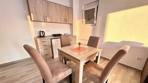 A modern kitchen with wooden cabinets, a dining table with four chairs, and a small window. - Apart-Hotel Saraj (Dobra Voda)