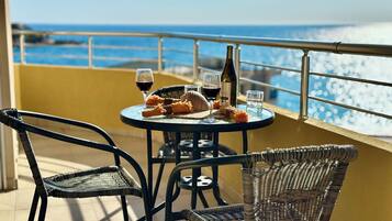 A round table with a bottle of wine, glasses, and bread on a balcony overlooking the sea.