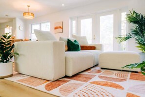 Una sala de estar moderna con sofá, reposapiés y un ventanal grande.