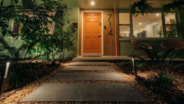 Una casa moderna con puerta de madera, un sendero de concreto y un jardín bien cuidado.