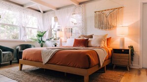 Un dormitorio con cama de madera, una mesita de noche, una silla y una ventana con cortinas.