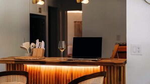 Una zona con barra de madera, una computadora portátil, una copa de vino y utensilios de cocina.