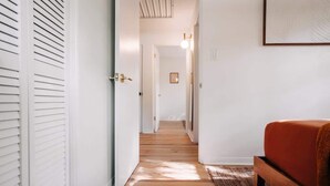 Un pasillo con suelo de madera, paredes blancas y una cama con cubrecama marrón.