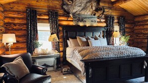 A log cabin bedroom with a large bed, a leather chair, and a deer head mounted on the wall. - Charming 3 bedroom Log cabin with WiFi in Kalispell (Kalispell)