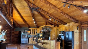 A rustic cabin interior with a wooden bar, seating area, kitchen, and a fireplace. - Charming 3 bedroom Log cabin with WiFi in Kalispell (Kalispell)