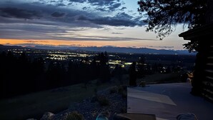 A hot tub with three people, surrounded by a view of a cityscape at dusk. - Charming 3 bedroom Log cabin with WiFi in Kalispell (Kalispell)